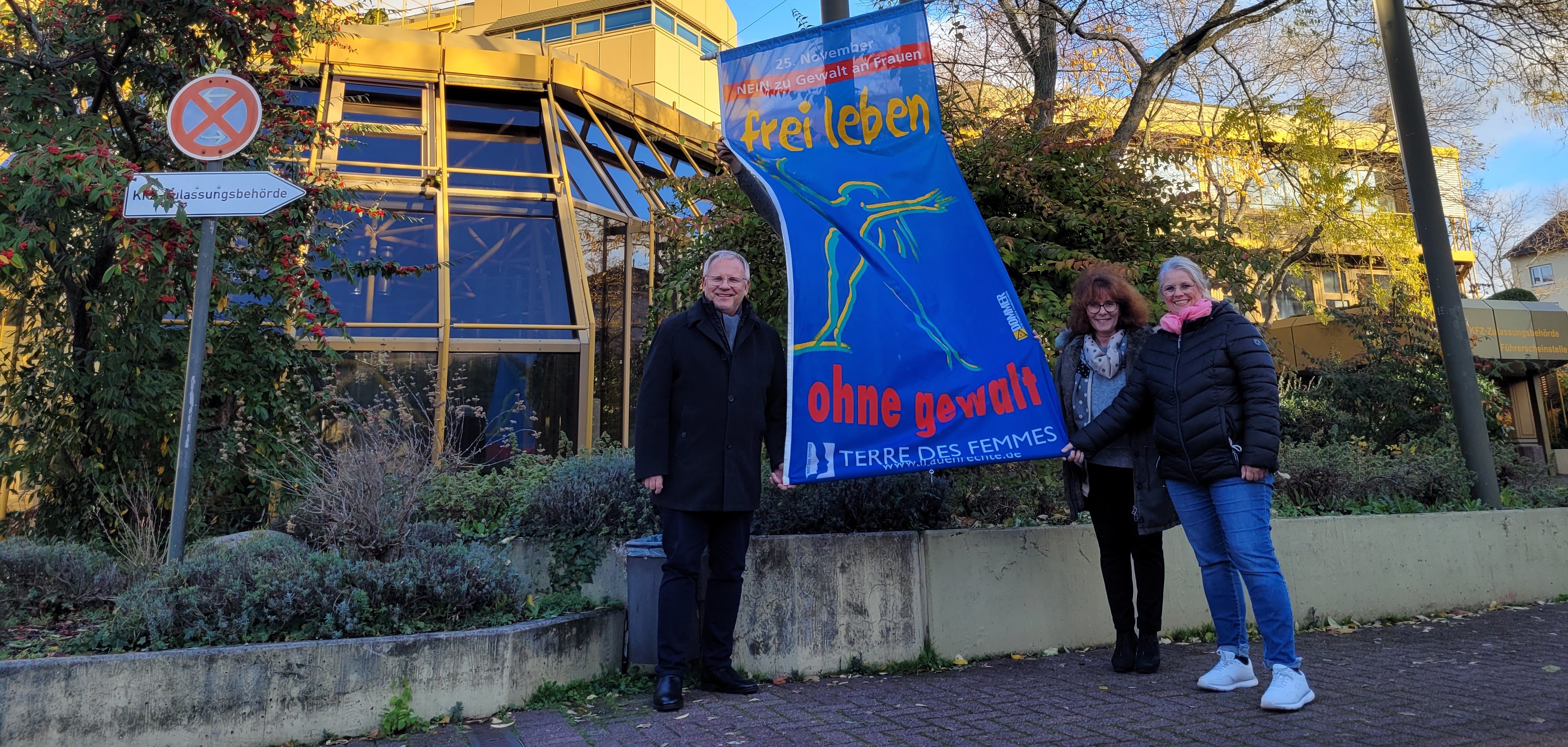 Landrat Ihlenfeld, Elke Thomas und Christina Koterba-Göbel hissen die Flagge von Terre des Femmes am Kreishaus (v.lil). 