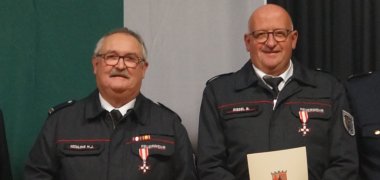 Geehrte Feuerwehrleute mit Urkunden auf einer Bühne vor einem dunklen Vorhang. 