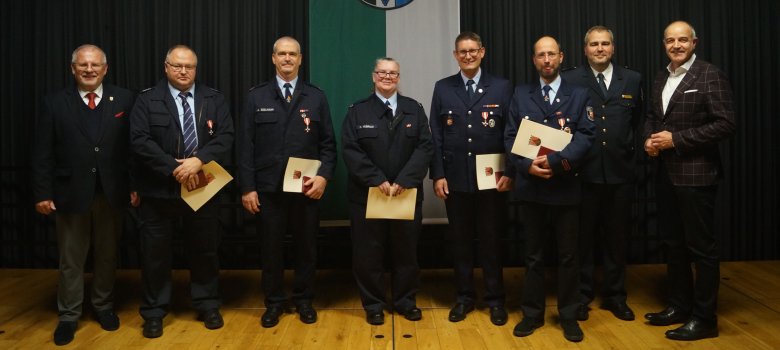 Geehrte Feuerwehrleute mit Urkunden auf einer Bühne vor einem dunklen Vorhang. 