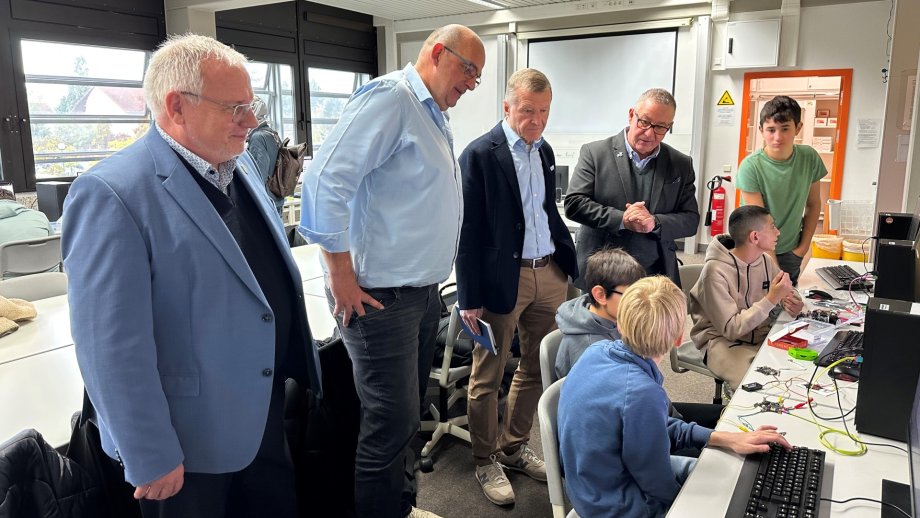 Landrat Hans-Ulrich Ihlenfeld, Lehrer Thomas Ehrmann, Gerhard Bugla, Rainer Bade stehen in einem Klassenraum. Vor ihnen sitzen drei Schüler vor Computern. Ein weiterer Schüler steht dabei.
