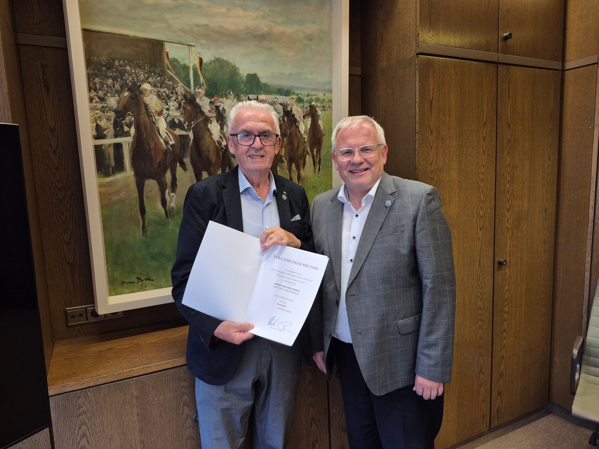 Zwei Männer, eine hält eine Urkunde.