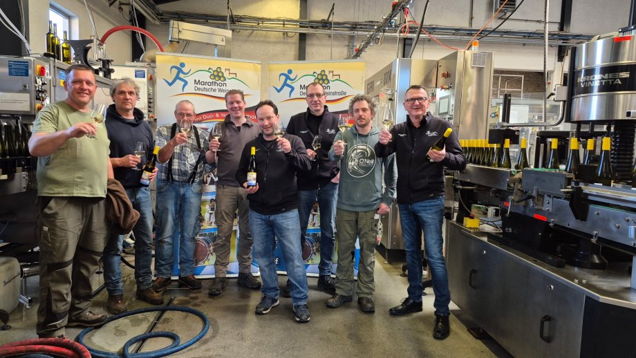 Mehrere Männer stehen neben einer Abfüllanlage und halten ein Glas in die Höhe.