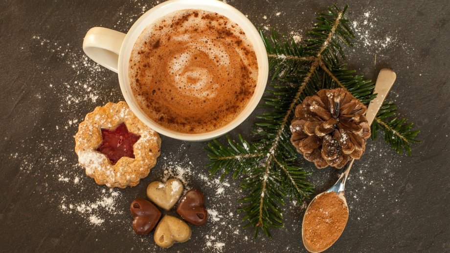 Eine Tasse mit heißer Schokolade, Plätzchen, Schokolade und Tannenzapfen auf dunklem Tisch. 