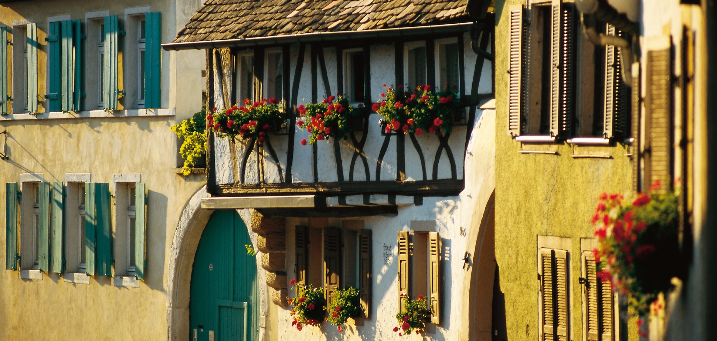 Ein altes Fachwerkhaus mit Blumenkästen und einem grünen Hoftor mit gemauertem Torbogen. 