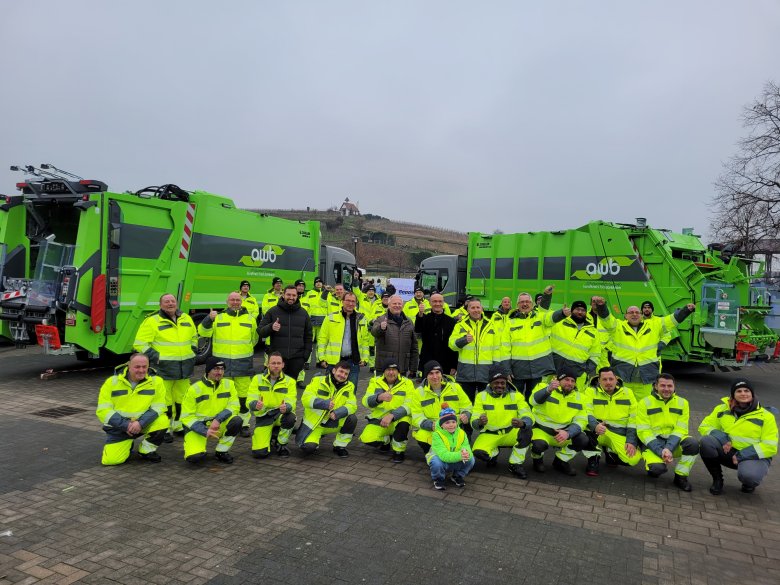 Ein Gruppenfoto vor zwei Müllfahrzeugen. 