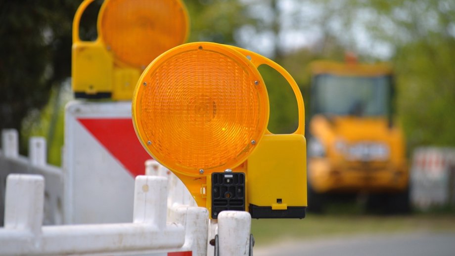 Warnleuchten an einer Baustelle, im Hintergrund ein gelbes Baustellenfahrzeug. 