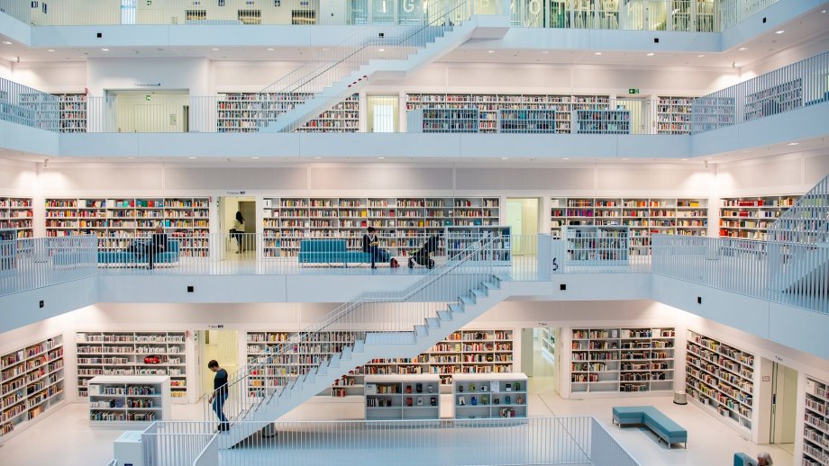Eine sehr helle Bücherei über mehrere Galerie-Etagen, die mit weißen Treppen miteinander verbunden sind.
