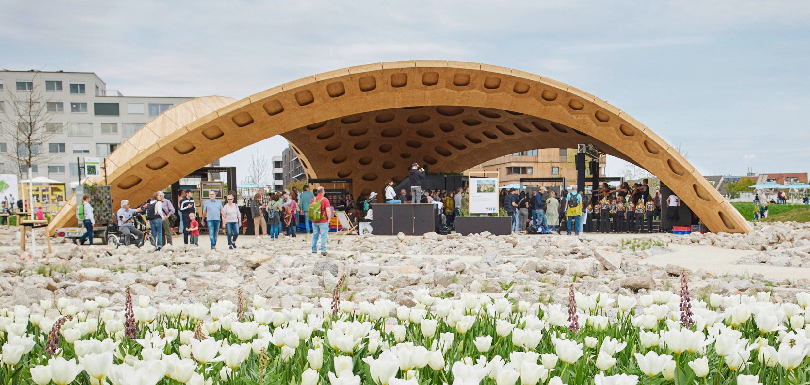 Der Pavillon der Metropolregion Rhein-Neckar auf der Bundesgartenschau in Mannheim ist eine große hölzerne Halbkugelförmige Konstruktion. Darin und drumherum halten sich Menschen auf. Davor blüht ein Tulpenmeer. 