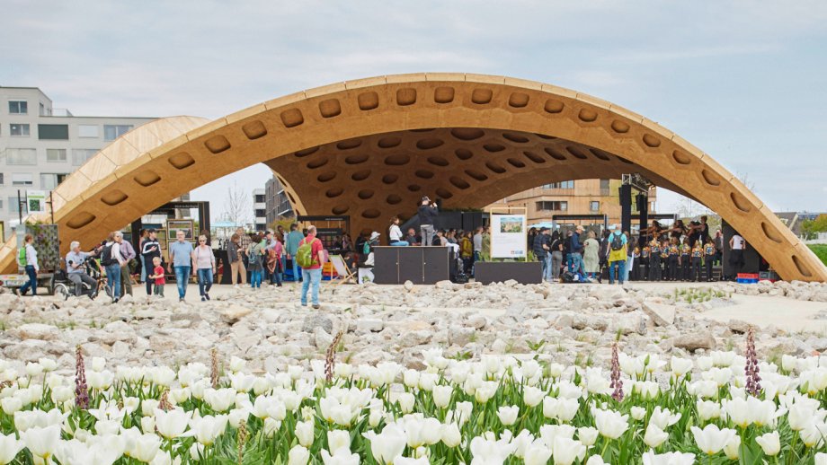 Der Pavillon der Metropolregion Rhein-Neckar auf der Bundesgartenschau in Mannheim ist eine große hölzerne Halbkugelförmige Konstruktion. Darin und drumherum halten sich Menschen auf. Davor blüht ein Tulpenmeer. 