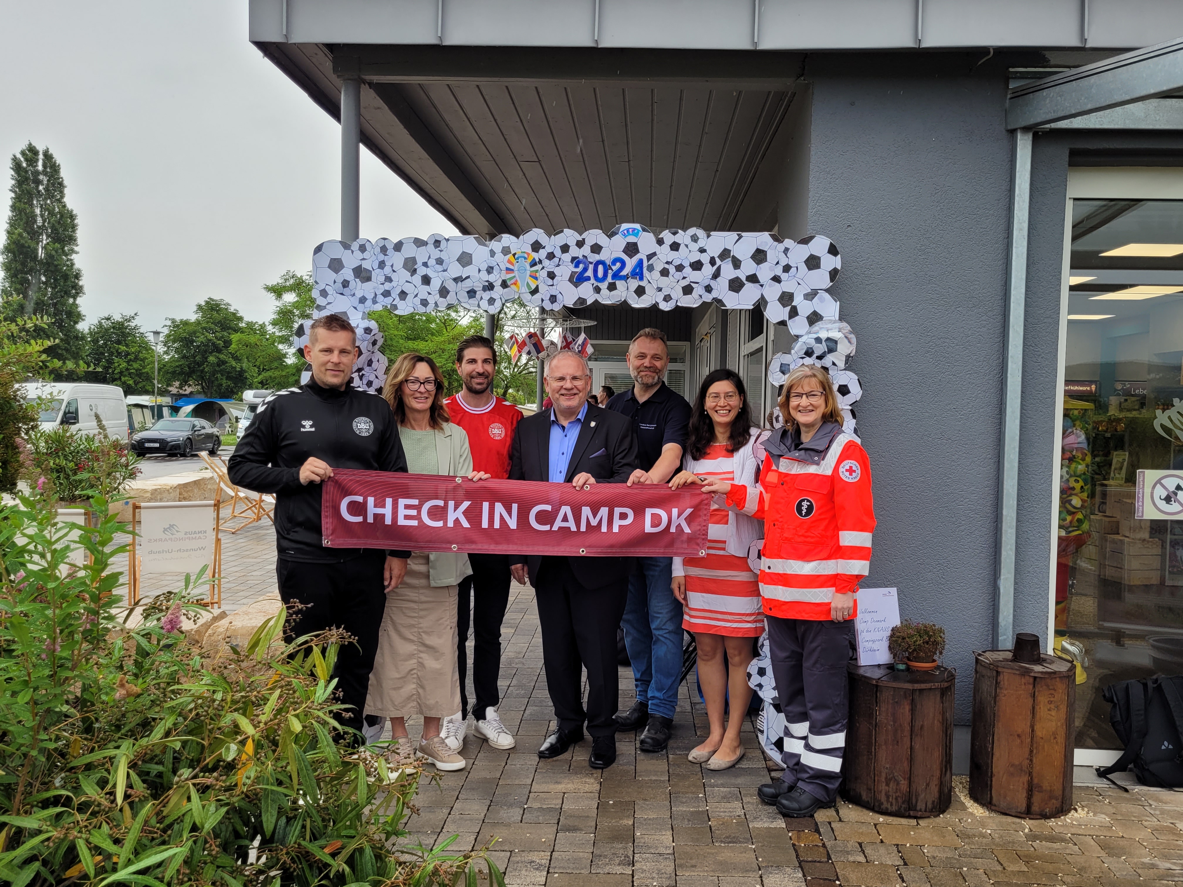 Eine Gruppe Menschen vor einem Deko-Fußball-Bogen mit einem Banner "Check In Camp DK".