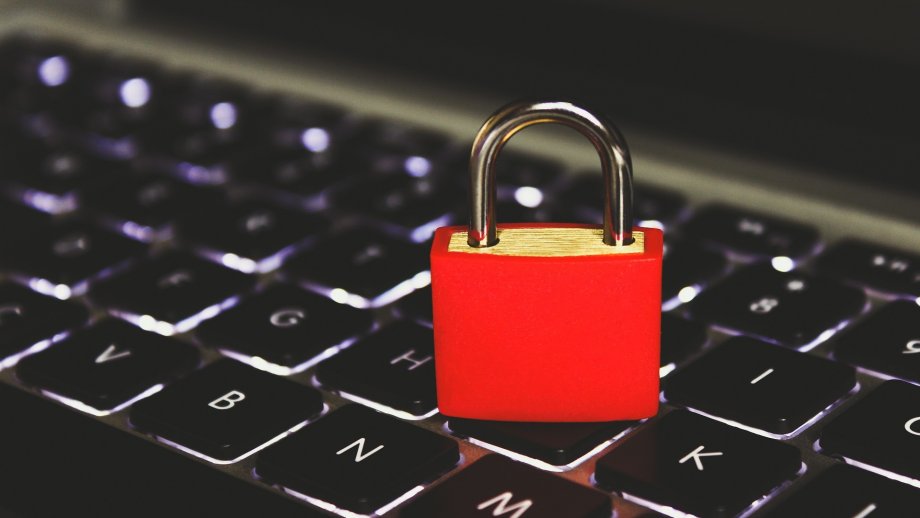 Auf einer schwarzen, leicht beleuchteten Tastatur steht ein rotes Vorhängeschloss.