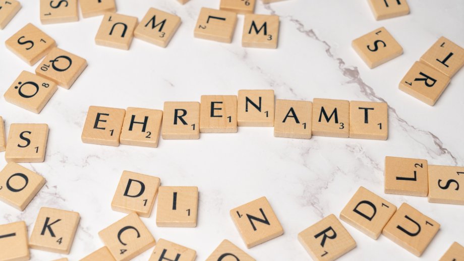Mit Buchstaben aus dem Spiel "Scrabble" ist das Wort Ehrenamt auf einem hellen Tisch gelegt. Drumherum liegen weitere Buchstaben. 