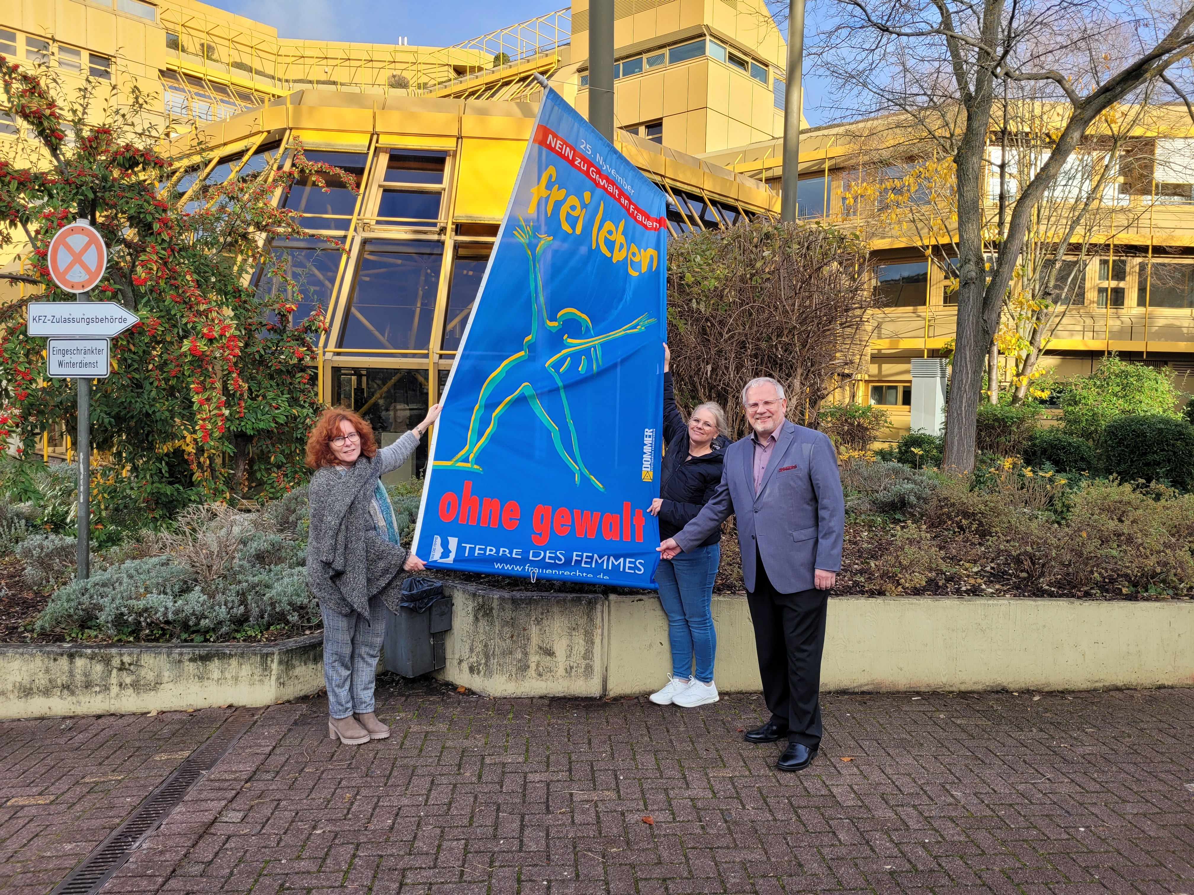 Zwei Frauen und ein Mann halten eine blaue Fahne mit der Aufschrift "Nein zu Gewalt an Frauen, Frei Leben ohne Gewalt". 