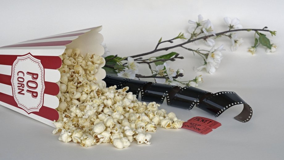 Neben einer umgekippten Popcorn-Tüte liegen ein Zweig mit Frühlingsblumen, ein Filmstreifen und ein Kino-Ticket.