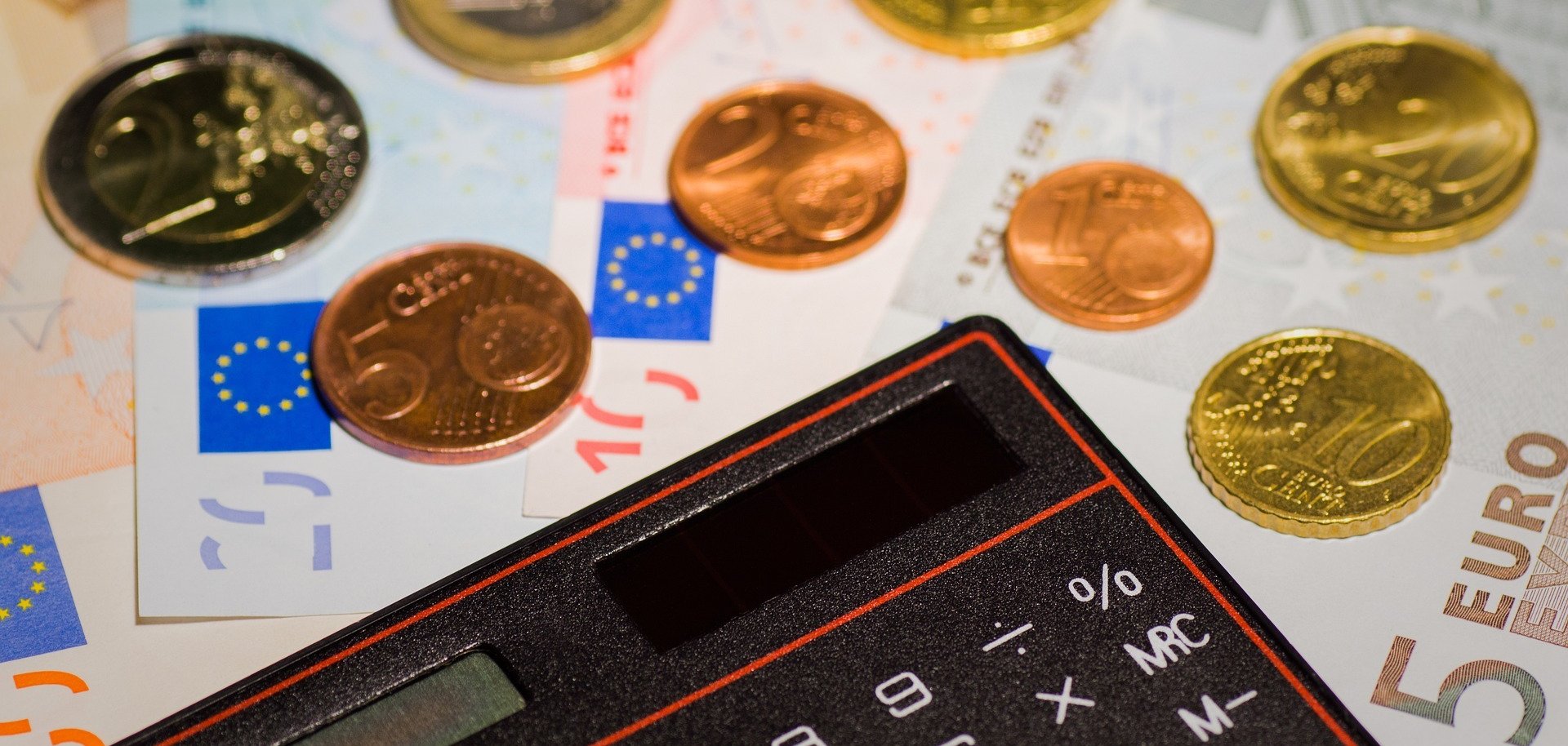 Um einen Taschenrechner liegen Münzen und Geldscheine. 