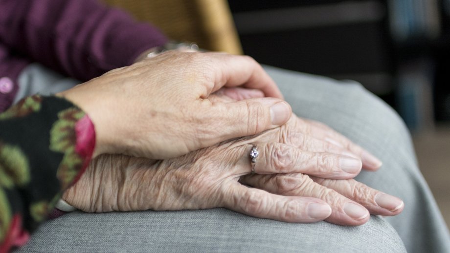 Eine jüngere Hand liegt auf den Händen einer Seniorin. 