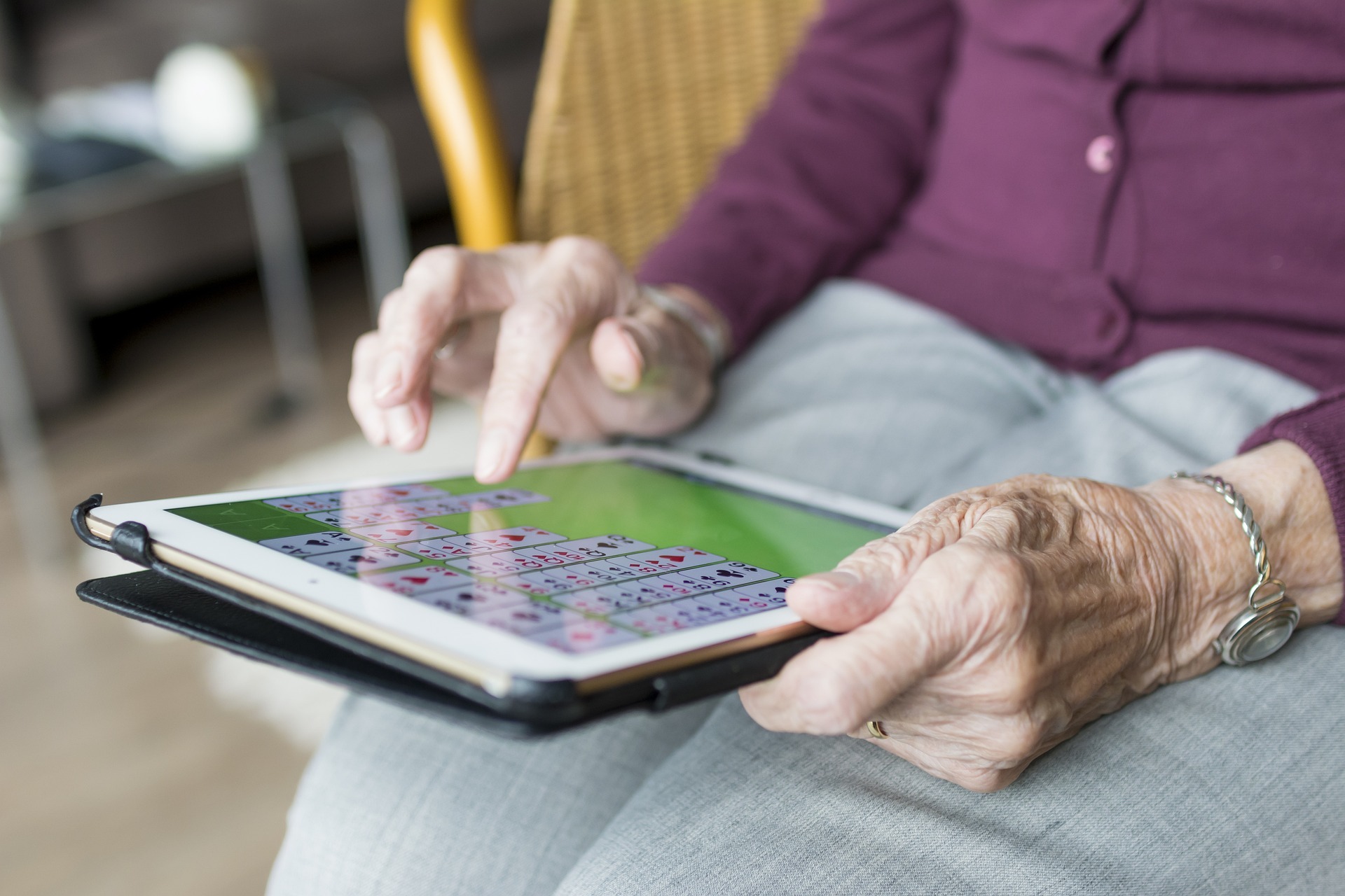Eine Seniorin hält ein Tablet und tippt gerade mit einem Finger auf den Bildschirm. 