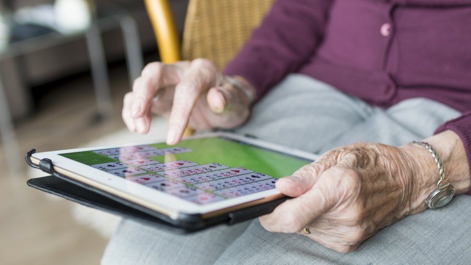 Eine Seniorin hält ein Tablet und tippt gerade mit einem Finger auf den Bildschirm. 