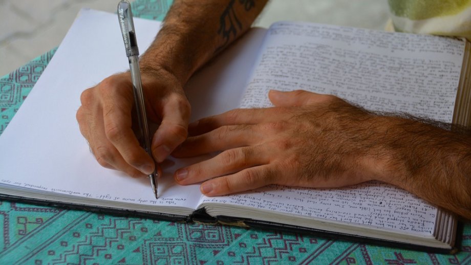 Eine Hand schreibt in ein Buch, die zweite Hand liegt daneben.