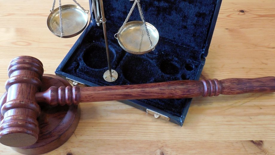 Der Hammer eines Richters und eine silbern glänzende Waage, die auf einem mit Samt ausgeschlagenen Köfferchen steht. 
