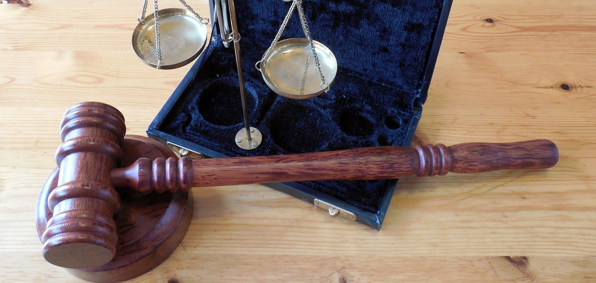 Der Hammer eines Richters und eine silbern glänzende Waage, die auf einem mit Samt ausgeschlagenen Köfferchen steht. 
