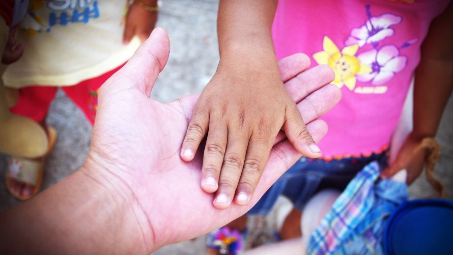 Eine Kinderhand liegt auf der Hand eines Erwachsenen. 