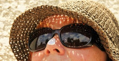 Frau mit Sonnenbrille und Strohhut mit Sonnencreme auf der Nase.