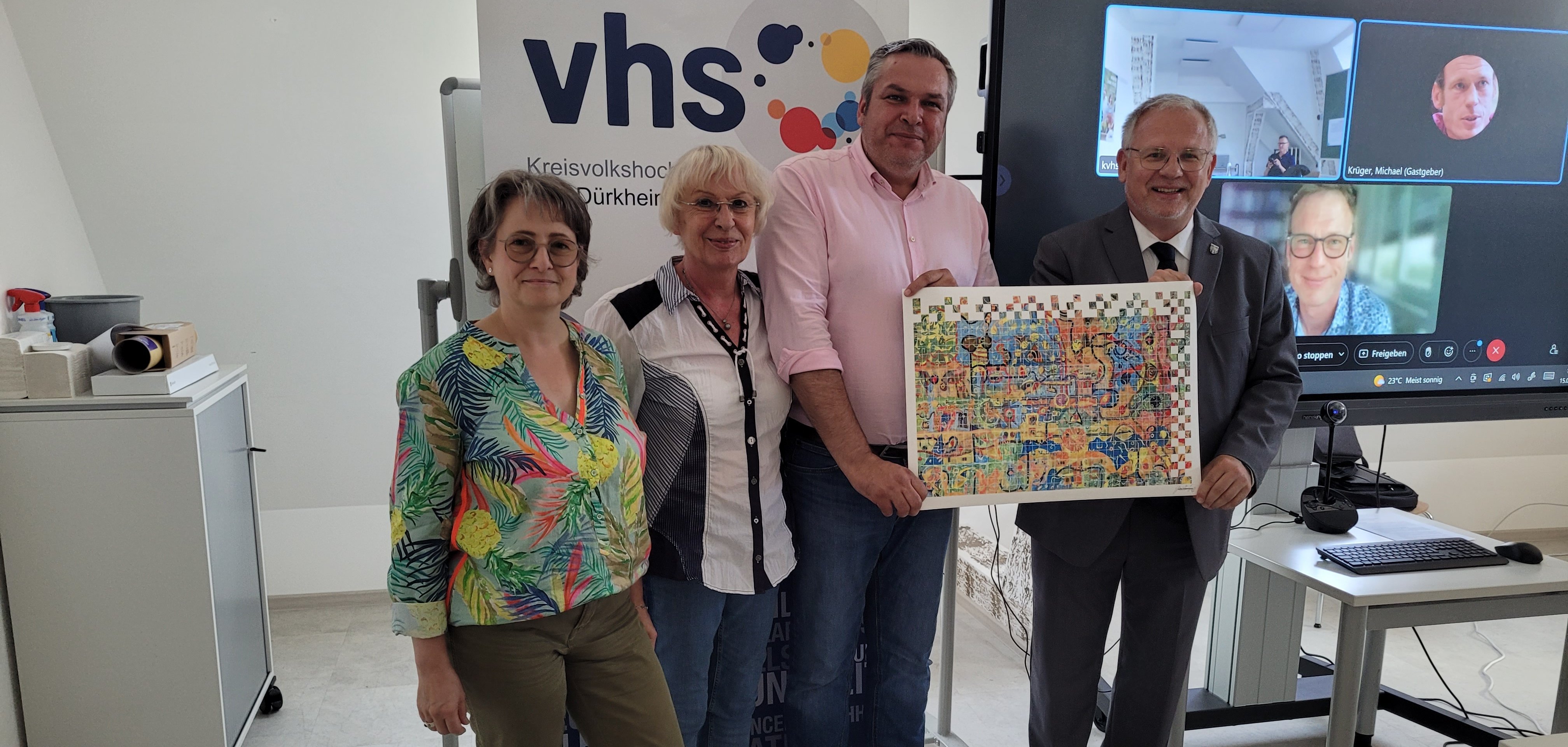 Zwei Frauen und zwei Männer mit einem Kunstdruck vor einem Bildschirm in einem Besprechungsraum. 