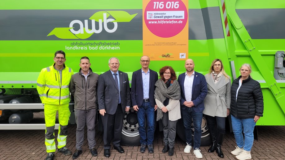 Eine Gruppe Menschen steht vor einem grünen Abfallsammelfahrzeug.