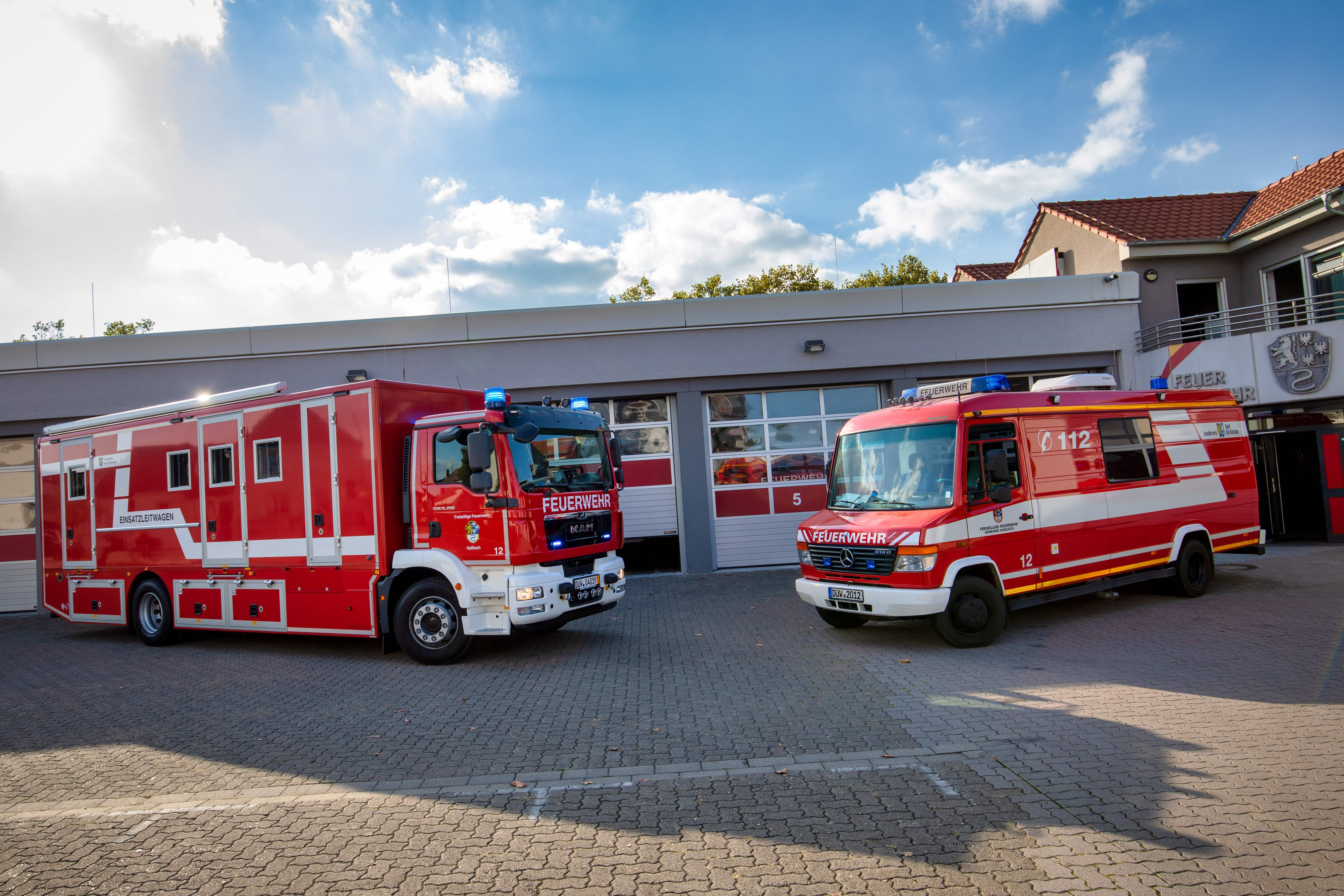 Zwei Einsatzleitwagen stehen vor einer Feuerwehr-Fahrzeughalle. 