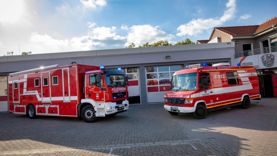 Zwei Einsatzleitwagen stehen vor einer Feuerwehr-Fahrzeughalle. 