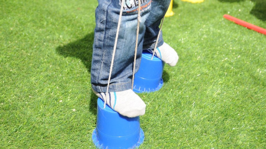 Beine und Füße eines Kindes in Jeans und Socken. Die Füße balancieren auf zwei kleinen, blauen, umgedrehten Eimern.