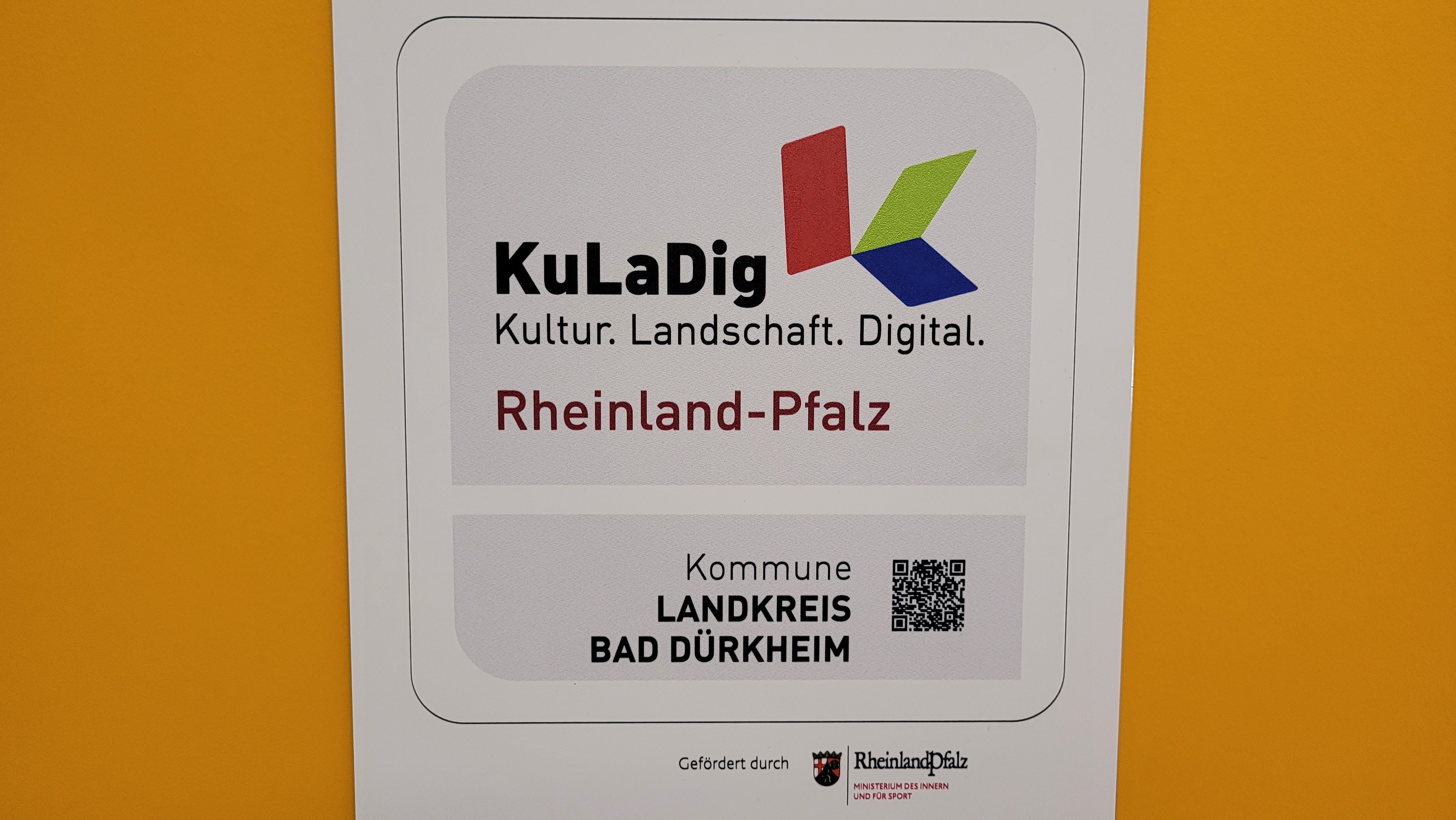 Die Kuladig-Plakette vor gelbem Hintergrund. 