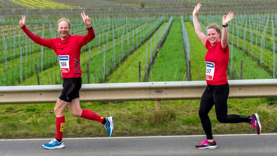 Mann und Frau in Laufkleidung jubeln, im Hintergrund Weinberge.