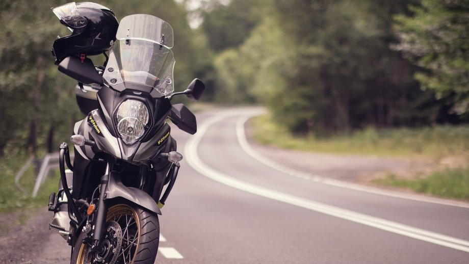 Ein Motorrad steht am Rand einer Landstraße, die eine Kurve macht. Links und rechts sind Bäume zu sehen. 