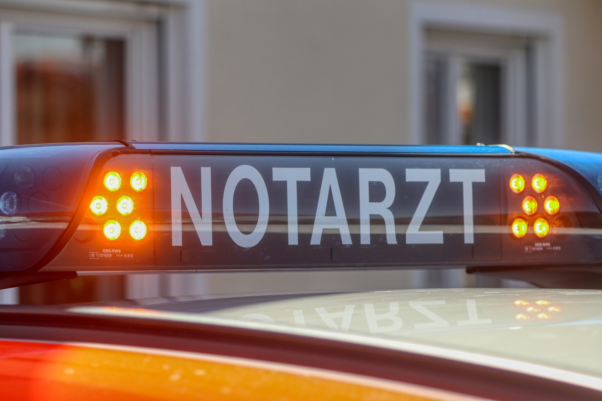 Ein blaues Notarzt-Schild mit orangefarbenen Blinklichtern auf einem Auto.