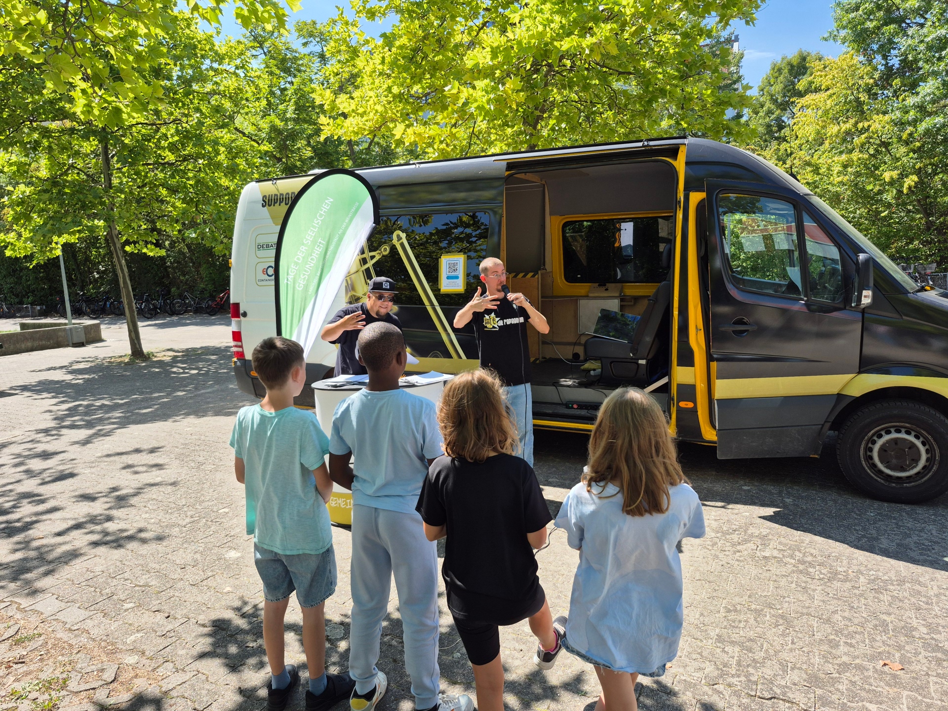 Vier Kinder, zwei Rapper vor einem Van.