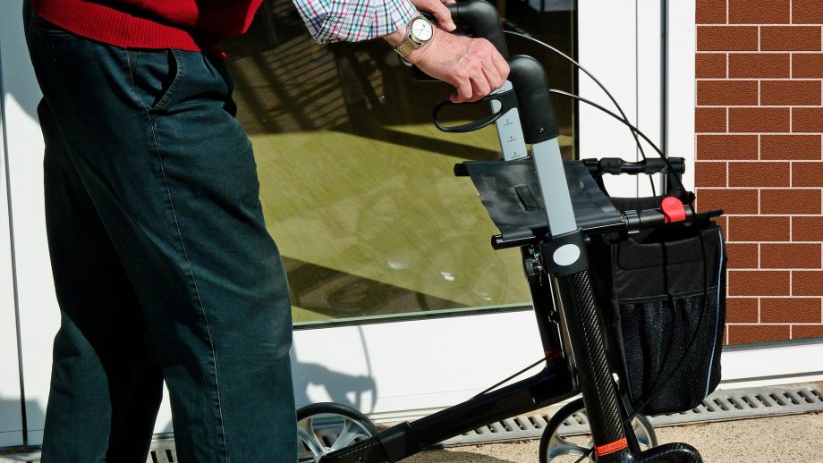 Ein Senior, dessen Kopf und Oberkörper nicht zu sehen sind, schiebt einen Rollator.