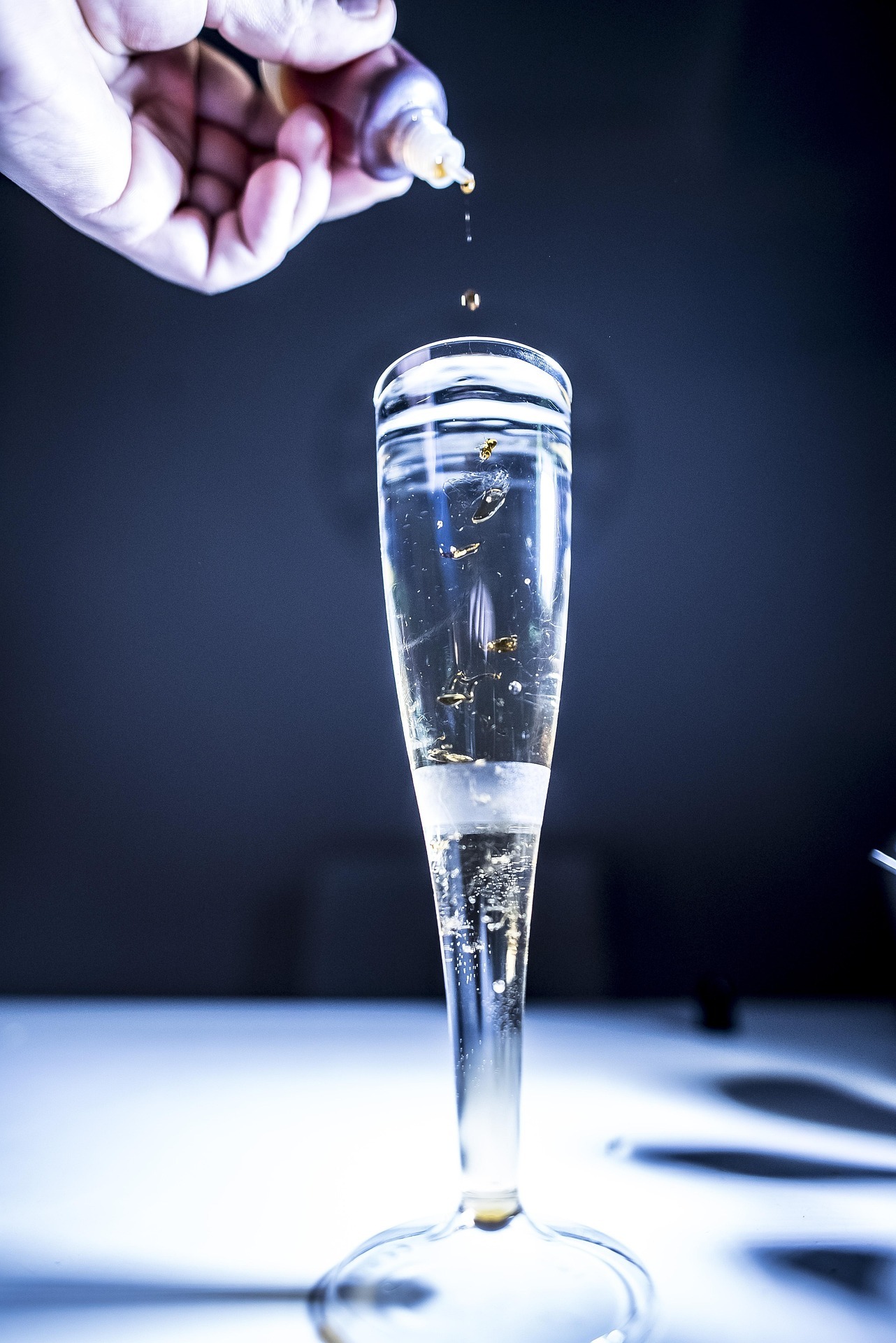Eine Hand hält ein Fläschchen, aus dem Tropfen in ein Glas fallen.