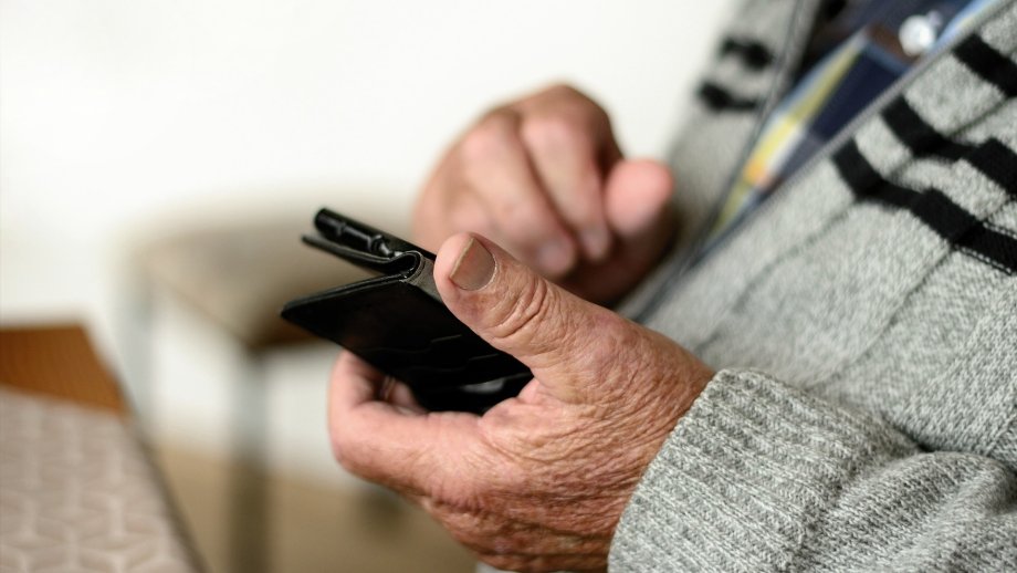Ein alter Mann, dessen Gesicht nicht zu sehen ist, hält ein Smartphone in der Hand. 