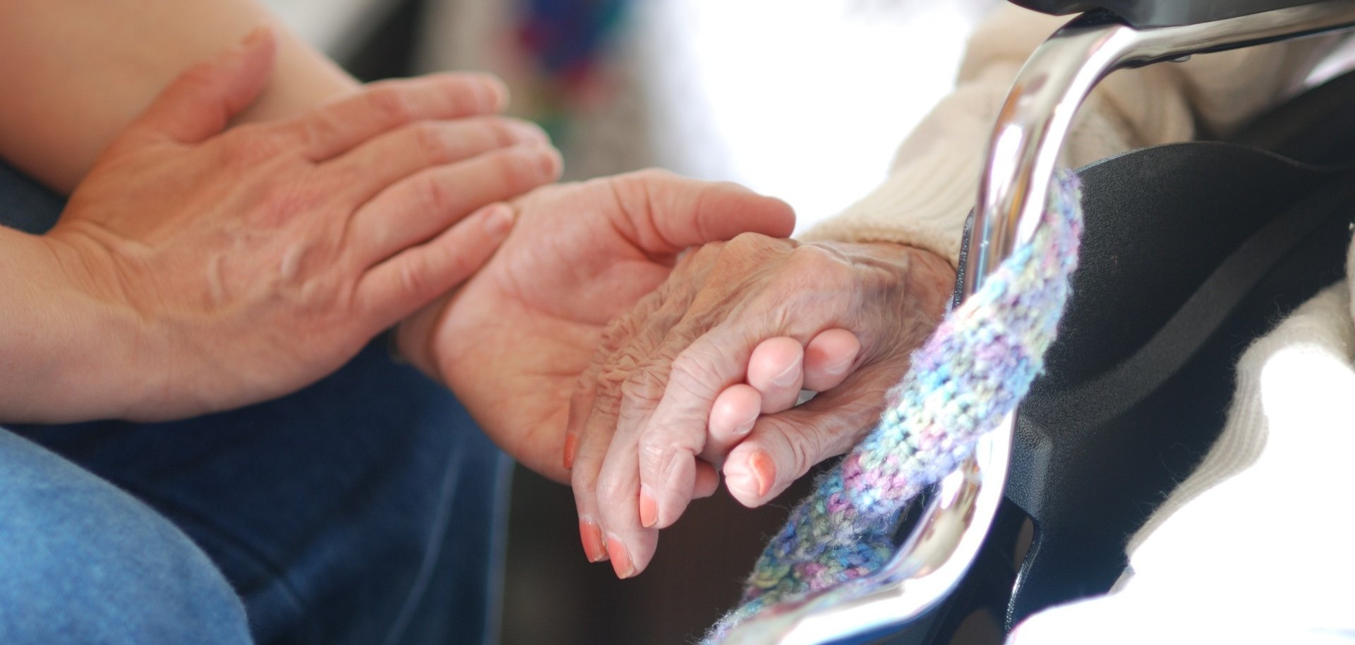 Zwei junge Hände halten eine Hand einer älteren Frau mit zartrosa lackierten Fingernägeln. 