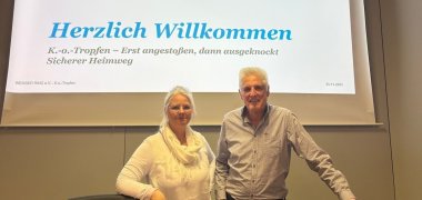 Eine Frau und ein Mann vor einer Leinwand mit Schrift.