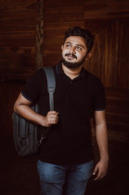 Mann schaut nach links oben, trägt einen Rucksack an einem Riemen über der Schulter.