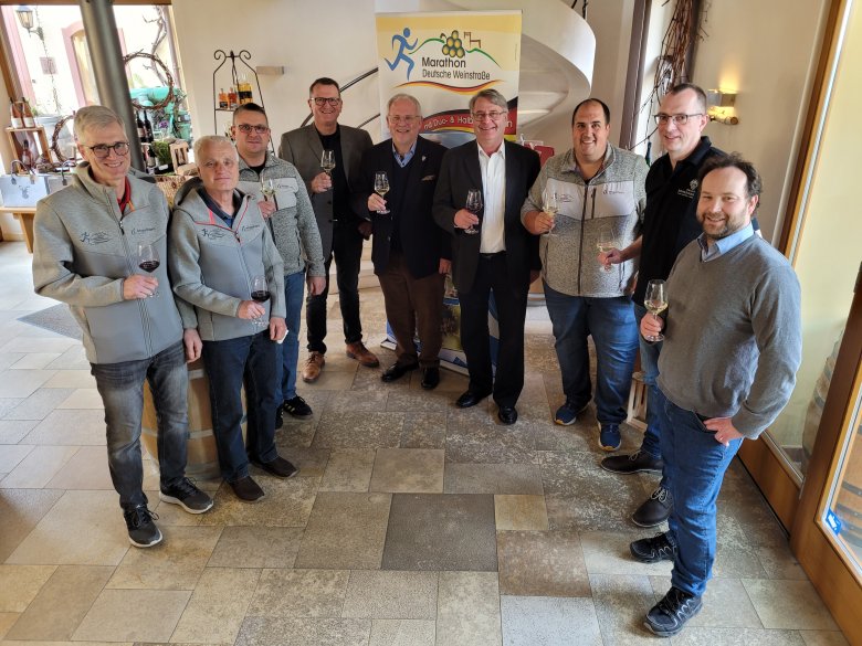 Männer stehen im Halbkreis und haben ein Glas Wein in der Hand.