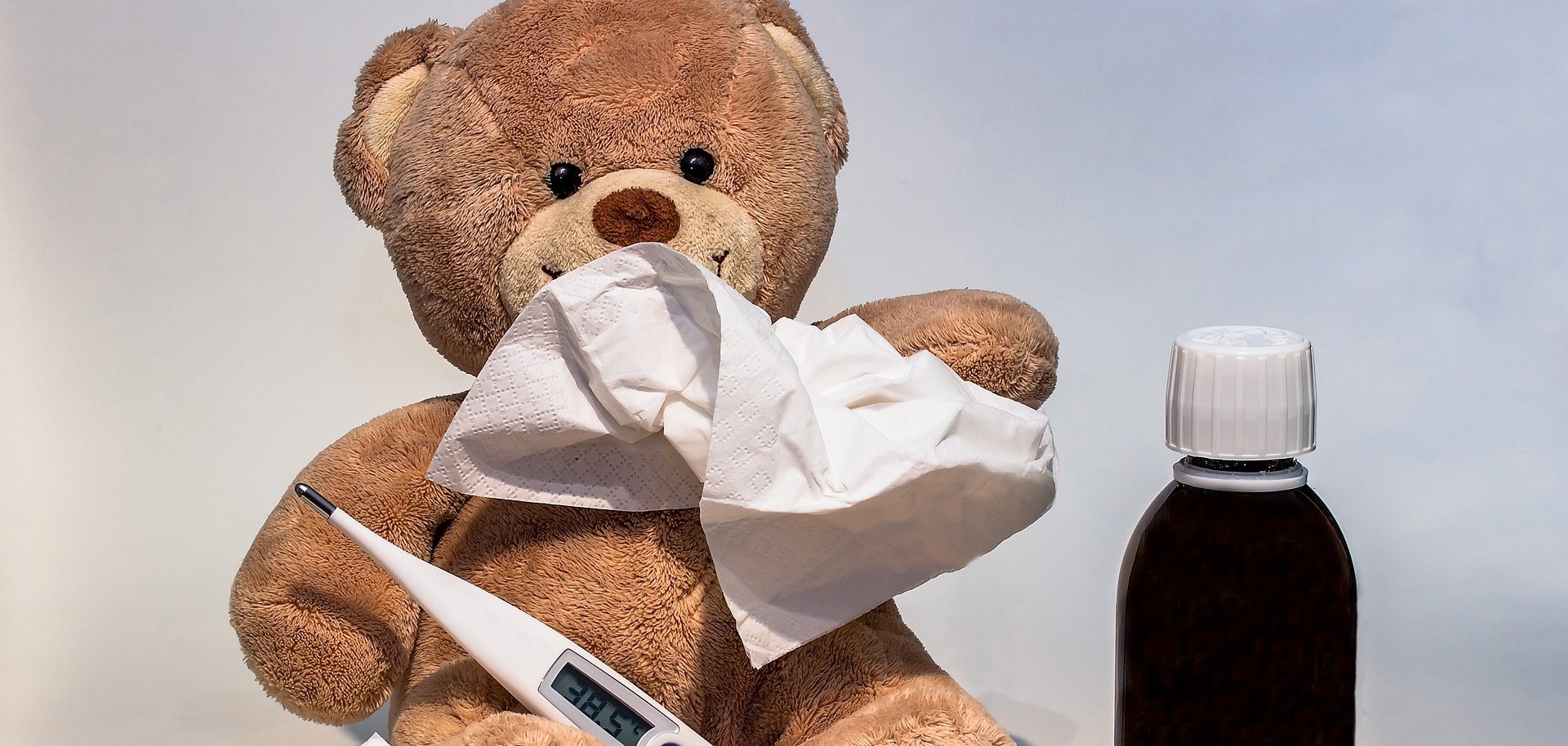 Teddybär mit Papiertaschentuch, Fieberthermometer und Medizin. 