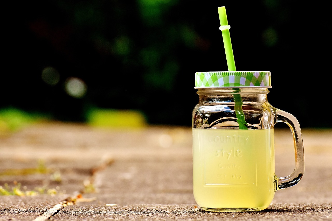 Ein Glas gelbe Limonade, das mit einem Deckel verschlossen ist, aus dem ein Strohhalm ragt. 