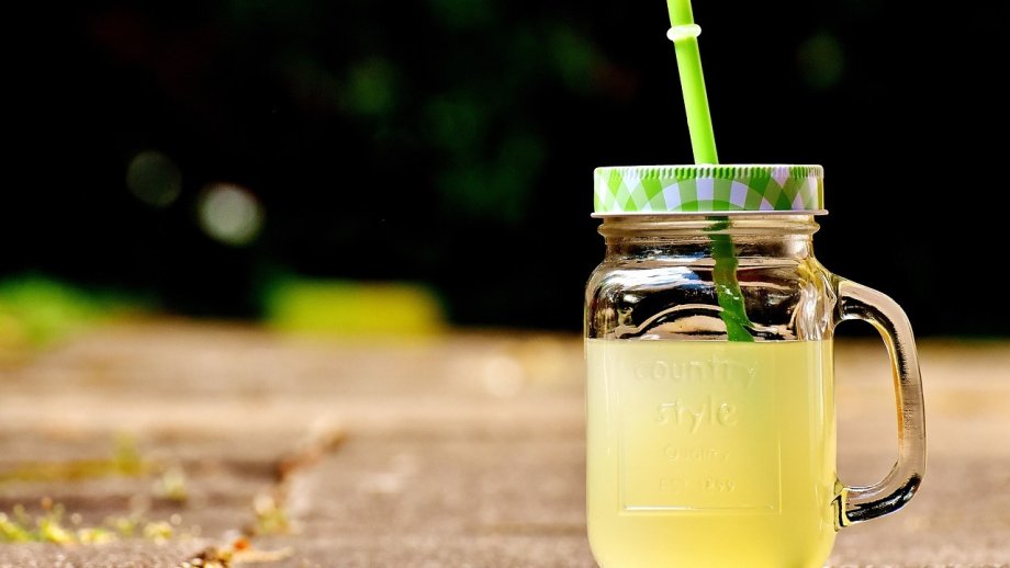 Ein Glas gelbe Limonade, das mit einem Deckel verschlossen ist, aus dem ein Strohhalm ragt.