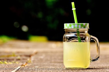 Ein Glas gelbe Limonade, das mit einem Deckel verschlossen ist, aus dem ein Strohhalm ragt.