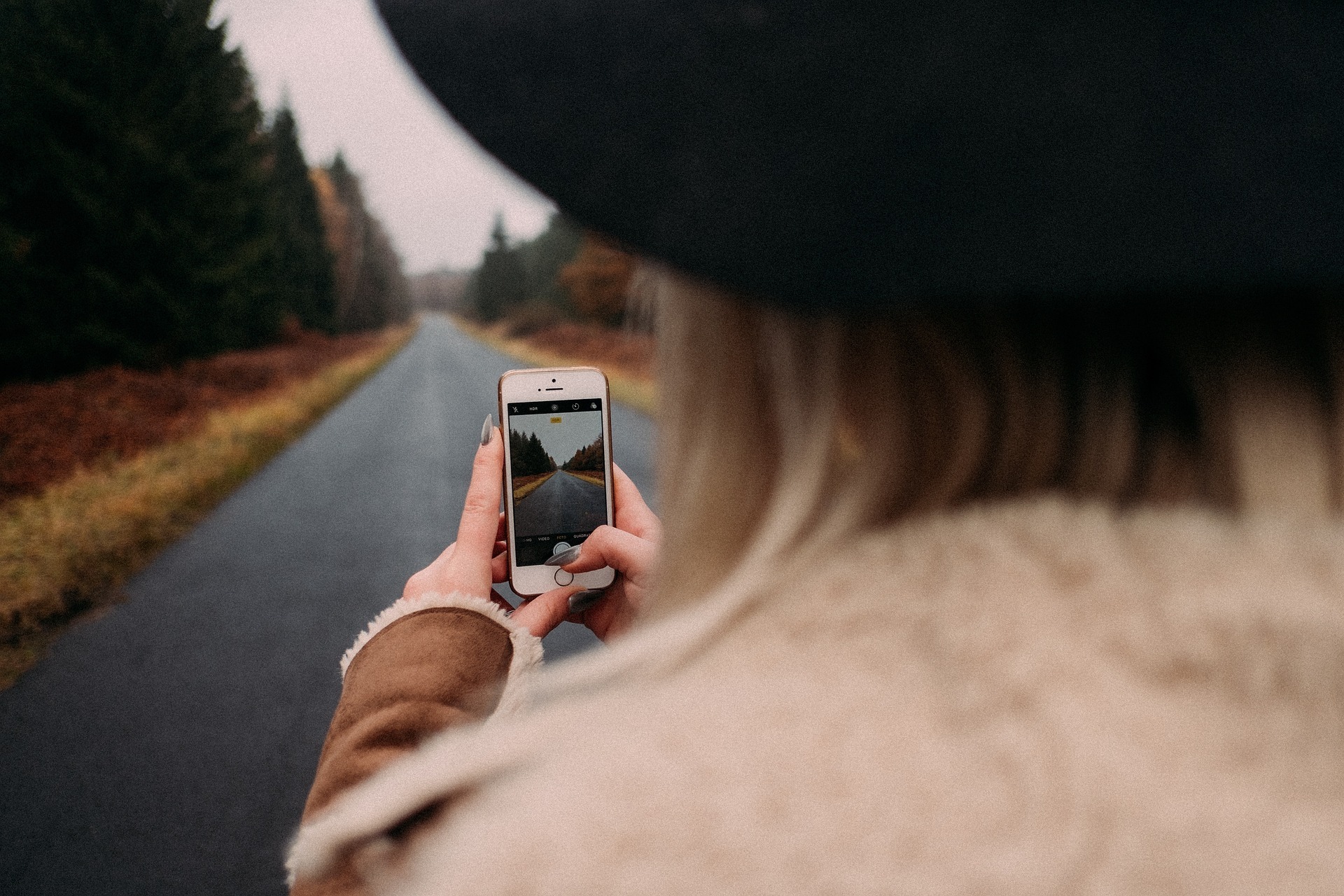 Frau mit Handy auf Straße im Wald.