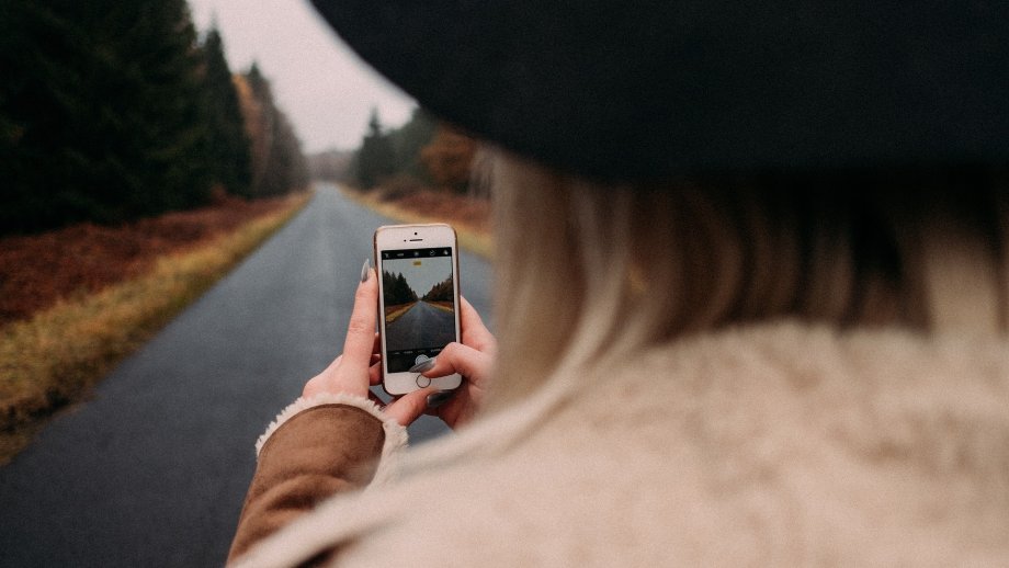 Frau mit Handy auf Straße im Wald.